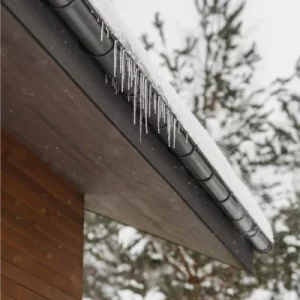 A house with a snow-covered roof and icicles hanging from the gutters, indicating winter-related gutter maintenance issues.